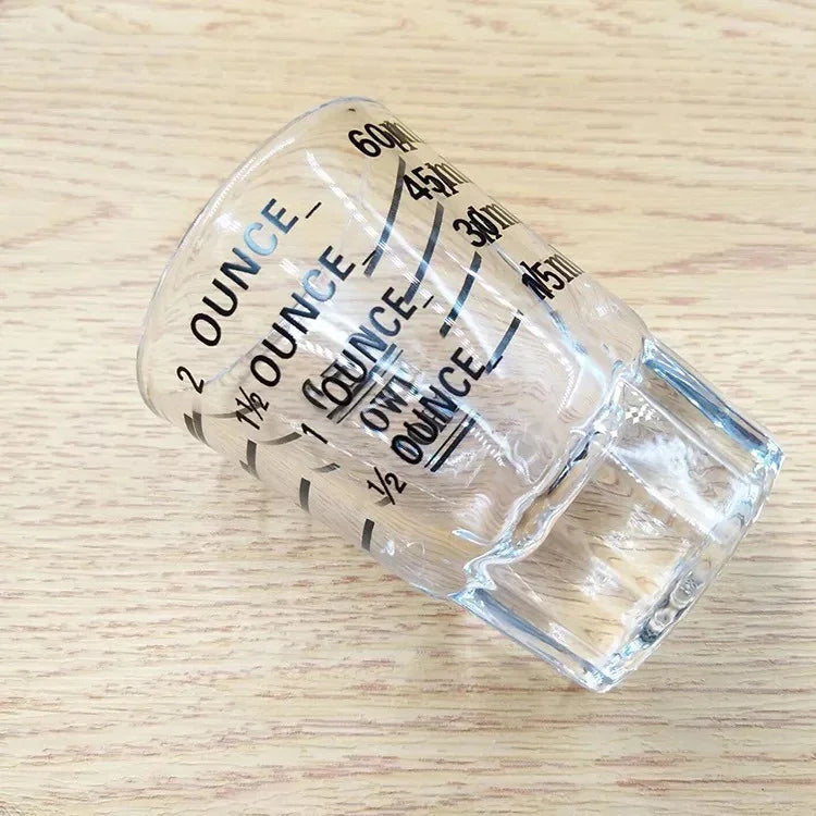 copo medidor de vidro transparente com marcações de onça e mililitros sobre superfície de madeira clara